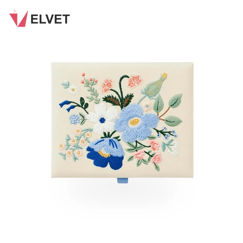 Top view of the hand-embroidered floral linen keepsake box lid showing the raised blue, white and pink thread bouquet on ivory linen
