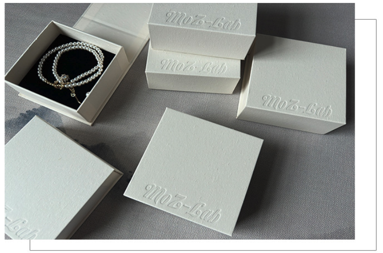 low moq jewelry boxes — a small-batch stack of white card boxes, one holding a bracelet