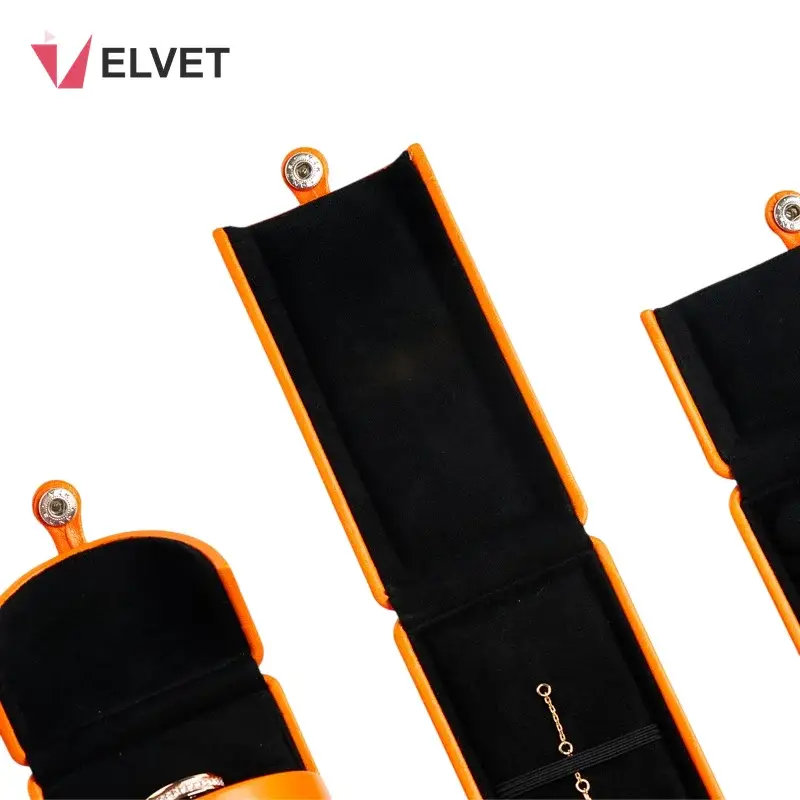 Long orange PU leather necklace box and a domed ring box open to reveal soft black velvet interiors, the long box holding a fine gold chain