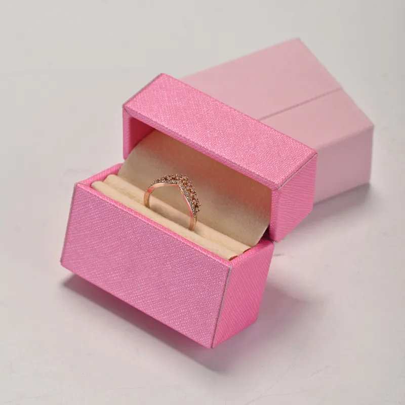 Hot pink saffiano PU leather ring box open on a clamshell hinge, showing a cream velvet ring slot holding a rose-gold pave wishbone ring, with a second closed box behind